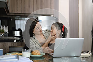 Beautiful working mom using a laptop and spending time with her little daughter at home