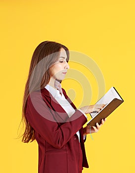 Beautiful working woman in red dress holding and looking diary  on yellow background