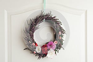 Beautiful wreath with heather flowers hanging on white wooden door. Space for text