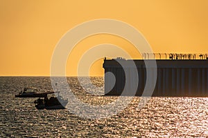 Beautiful yellow sunset over the sea. The sun goes down over the sea. Silhouette of a pier with fishermen at sunset