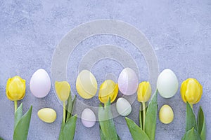Beautiful yellow tulips with colorful easter eggs on concrete background.
