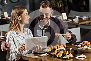 Beautiful young adult couple using digital tablet while having dinner