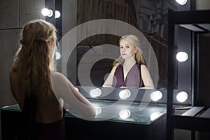 Beautiful young adult woman blonde looking at her reflection in a dressing room mirror