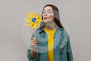 Beautiful young adult woman blowing at paper windmill, pinwheel toy on stick.