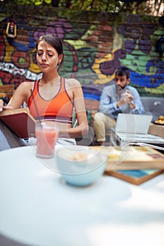 Beautiful young adult woman sitting in outdoor cafe, reading a book