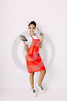 Beautiful young African American beautician woman holding set of make up brushes and eye-shadows, isolated on white