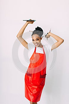 Beautiful young African American beautician woman holding set of make up brushes and eye-shadows, isolated on white