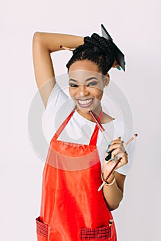 Beautiful young African American beautician woman holding set of make up brushes and eye-shadows, isolated on white