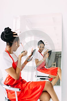 Beautiful young African American beautician woman holding set of make up brushes and watching in the mirror