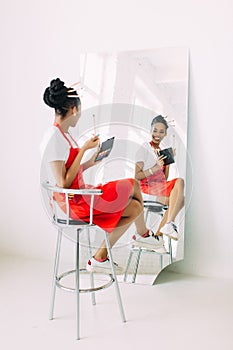 Beautiful young African American beautician woman holding set of make up brushes and watching in the mirror