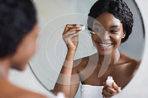 Beautiful young african american lady using facial serum