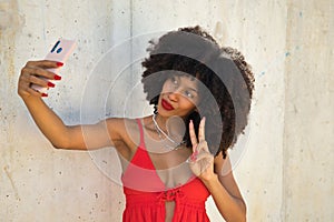 Beautiful young african american woman with afro hair with coral top and white skirt taking a selfie