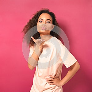 Beautiful young African American woman with Afro hair sending air kisses, looking positively at camera wearing peachy t