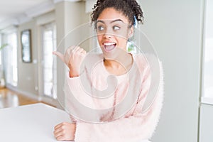 Beautiful young african american woman with afro hair smiling with happy face looking and pointing to the side with thumb up