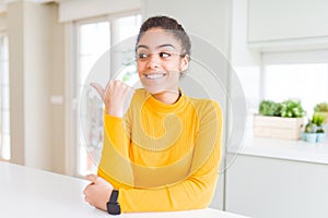 Beautiful young african american woman with afro hair smiling with happy face looking and pointing to the side with thumb up