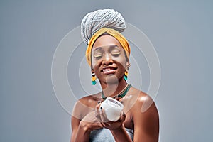 Beautiful young African American woman applying cream on skin on grey background