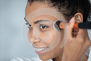 Beautiful young african american woman applying foundation.