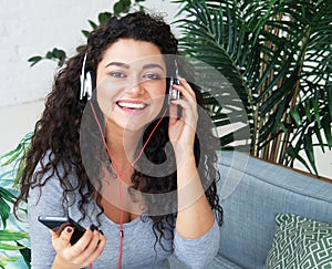 Beautiful Young African American woman dressed casual listen to music and sitting on the sofa at home.