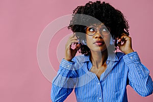 beautiful young African american woman listening music in headphones  on pink background