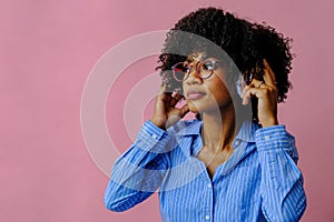 beautiful young African american woman listening music in headphones  on pink background