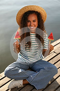 Beautiful young African American woman with pieces of watermelon on wooden pier near river
