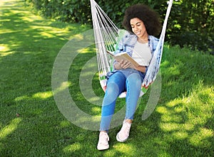 Beautiful young African-American woman reading book in hammock outdoors