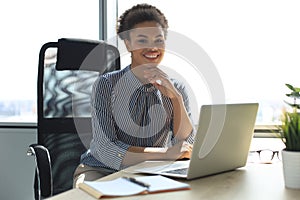 Beautiful young african american woman is sitting in the office and looking at camera