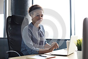 Beautiful young african american woman is sitting in the office and looking at camera