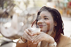 Beautiful young african american woman sitting in outdoor cafe and drinking coffee