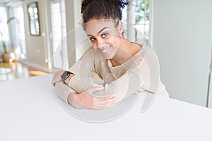 Beautiful young african american woman smiling cheerful leaning on the table comfortable