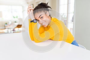 Beautiful young african american woman smiling cheerful leaning on the table comfortable