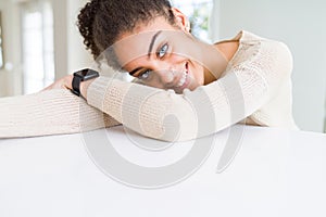 Beautiful young african american woman smiling cheerful leaning on the table comfortable