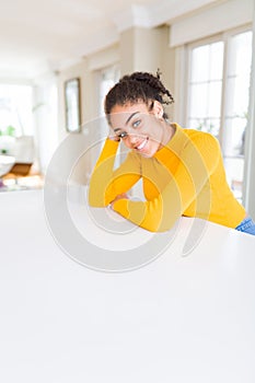 Beautiful young african american woman smiling cheerful leaning on the table comfortable