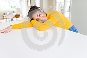 Beautiful young african american woman smiling cheerful leaning on the table comfortable