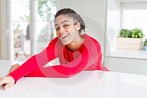 Beautiful young african american woman smiling cheerful leaning on the table comfortable