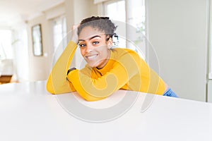 Beautiful young african american woman smiling cheerful leaning on the table comfortable