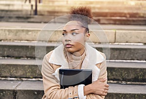 beautiful young african american woman student sitting at a steps in the city with notebook making study plans