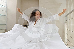 Beautiful young African American young woman stretching in the bed while waking up in the morning