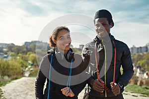 Beautiful young african couple in sportswear holding jumping ropes, looking at camera and smiling while working out