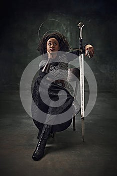 Beautiful young African girl, medieval warrior in chainmail armor with halo-like rings above head sitting on chair