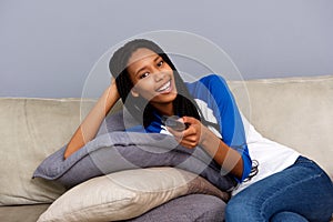 Beautiful young african woman holding remote control relaxing on at sofa and watching tv