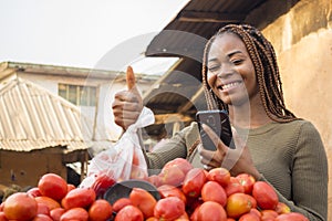 beautiful young african woman in a local african market using her smartphone giving thumbs up