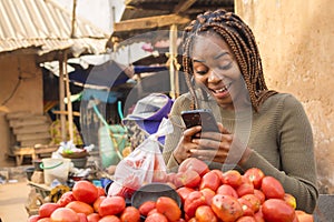 beautiful young african woman in a local african market viewing content on her phone looking surprised