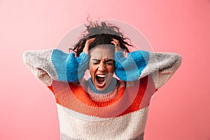 Beautiful young african woman posing isolated over pink wall background screaming