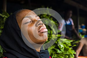 beautiful young african woman with scarf and eyes closed and natural face with head tilted up relaxing herself and clearing her