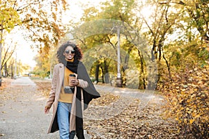 Beautiful young african woman walking outdoors in a spring park drinking coffee