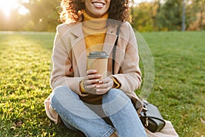 Beautiful young african woman walking outdoors in a spring park drinking coffee