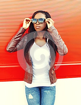 Beautiful young african woman wearing a jacket, sunglasses in city over red