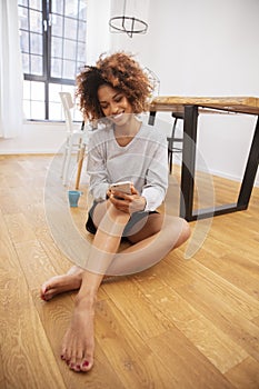 Beautiful young afro american woman texting on mobile phone at home.