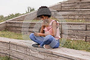 Beautiful young afro american woman using mobile phone, Sitting on wood stairs and smiling. wood background. Lifestyle outdoors